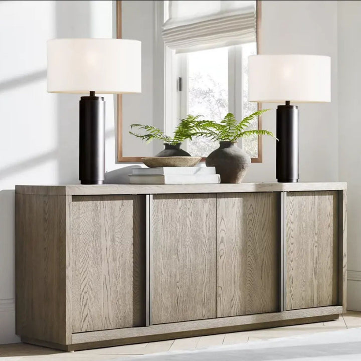 Två bordslampor Atlas i svart med vita tygskärmar placerade symmetriskt på sideboard i vardagsrum