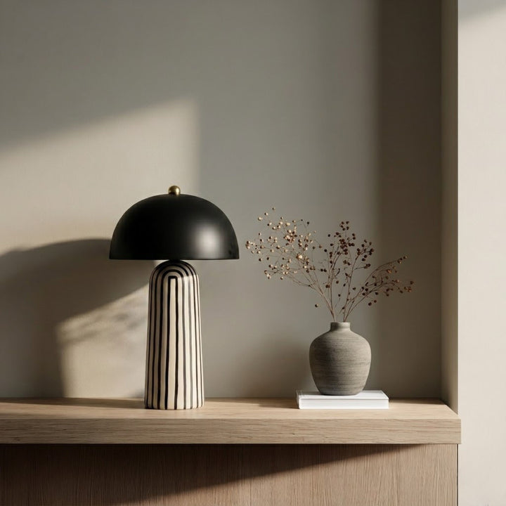 Bordslampa Cavern Zebra med randig fot och svart skärm på hylla med vas i mjukt ljus