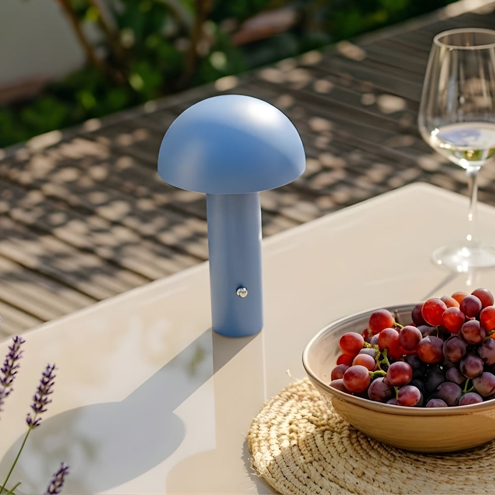 De Mesa portabel bordslampa i blå färg placerad på bord utomhus med druvor och glas, i varm och stilren skandinavisk miljö.