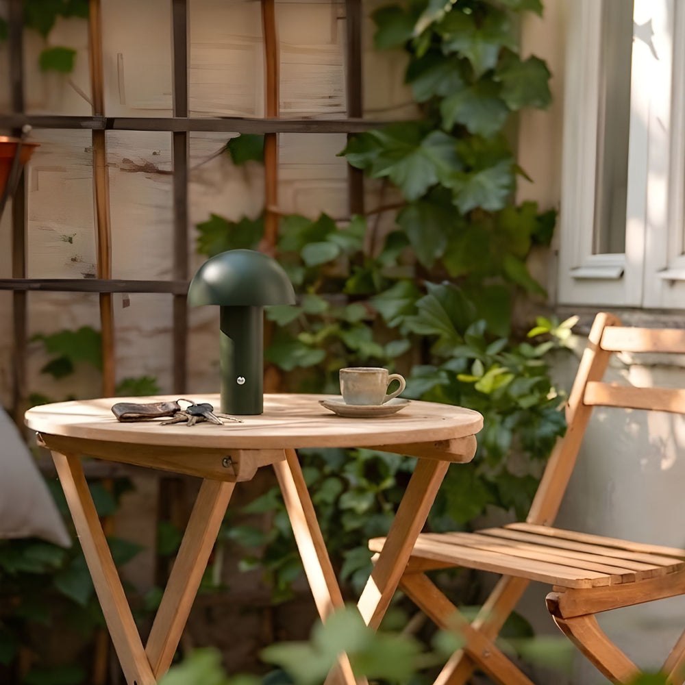 De Mesa portabel bordslampa i grön färg på runt cafébord utomhus med kopp och naturliga material i en harmonisk skandinavisk utemiljö.