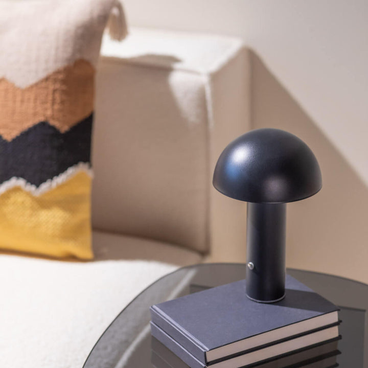 Svart bordslampa De Mesa på bokstapel i stilrent vardagsrum med mjuka textilier