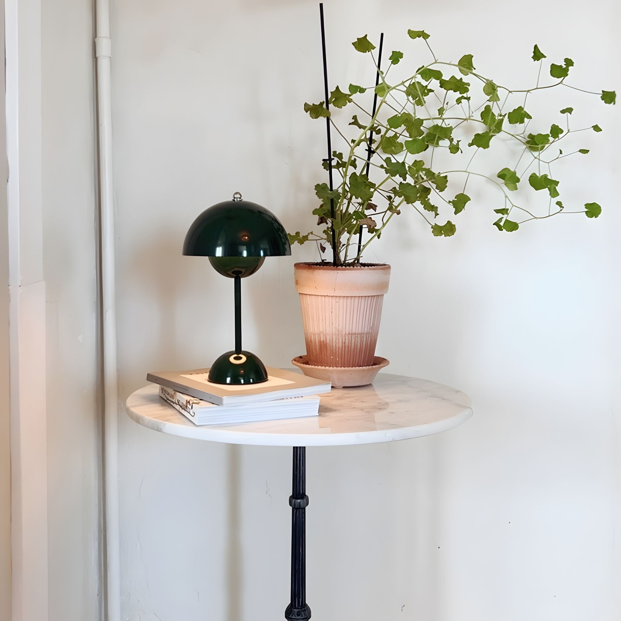 Flowerbud bordslampa i grön färg med minimalistisk design, placerad på runt sidobord tillsammans med växt i ljus och stilren inredning