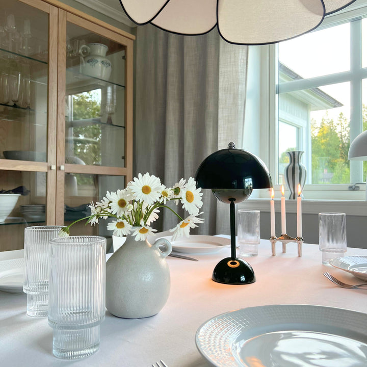 Flowerbud bordslampa i grön finish med rund skärm, placerad på dukat matbord med blommor och ljus i stilren skandinavisk miljö
