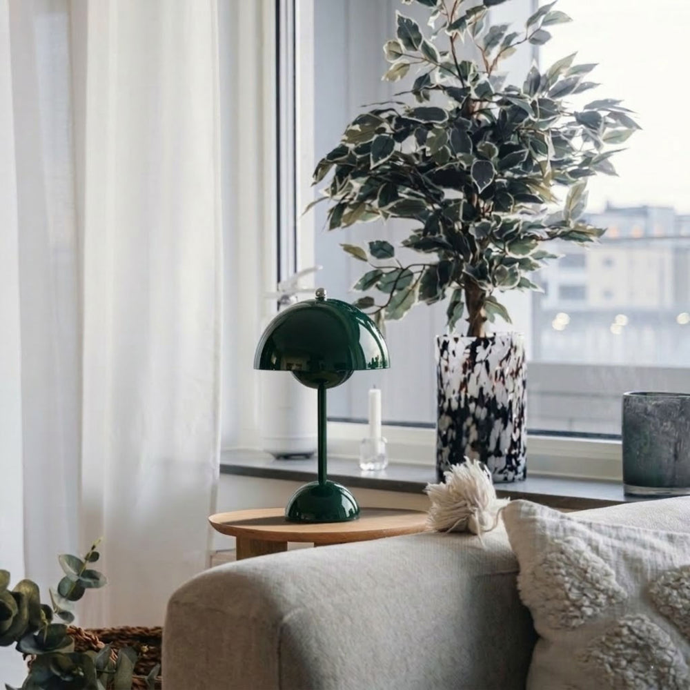 Flowerbud bordslampa i mörkgrön finish med rund skärm, placerad på sidobord vid fönster i stilrent vardagsrum med skandinavisk inredning och växter