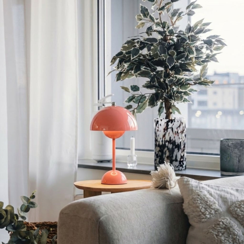 Flowerbud bordslampa i rosa finish med rund skärm, placerad på sidobord vid fönster i stilrent vardagsrum med skandinavisk inredning och gröna växter