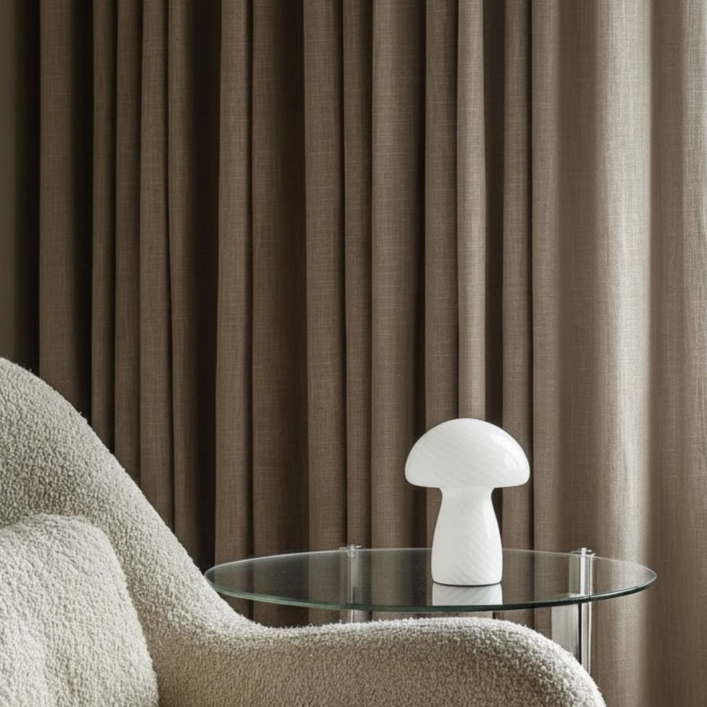 Bordslampa Fungo på sidobord bredvid fåtölj i lugnt vardagsrum med textilier och varm, modern känsla.