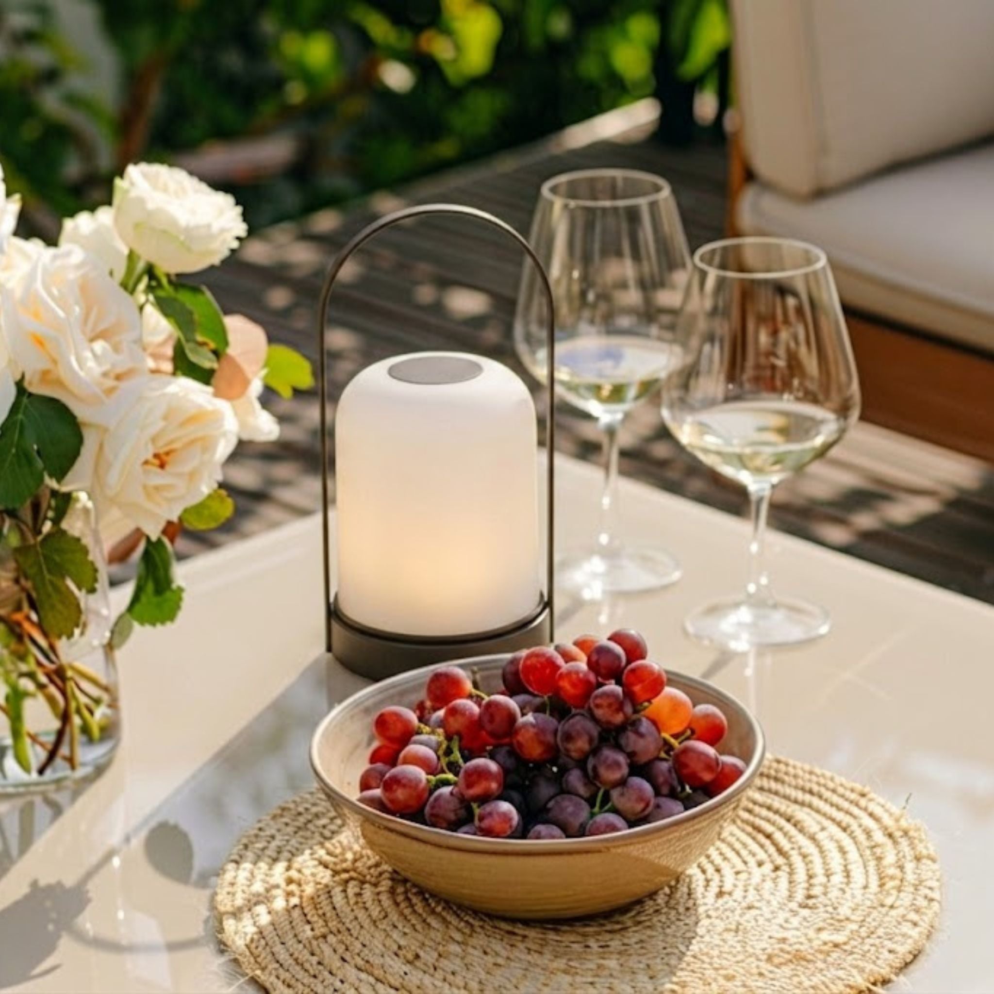 Portabel bordslampa Halo på terrassbord med blommor, druvor och vinglas i dagsljus