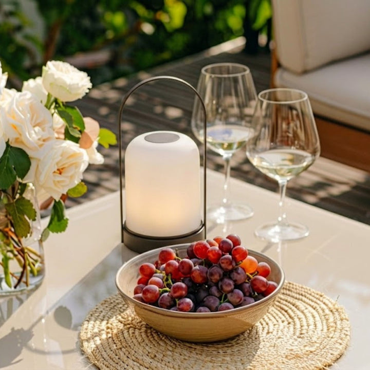 Portabel bordslampa Halo på terrassbord med blommor, druvor och vinglas i dagsljus