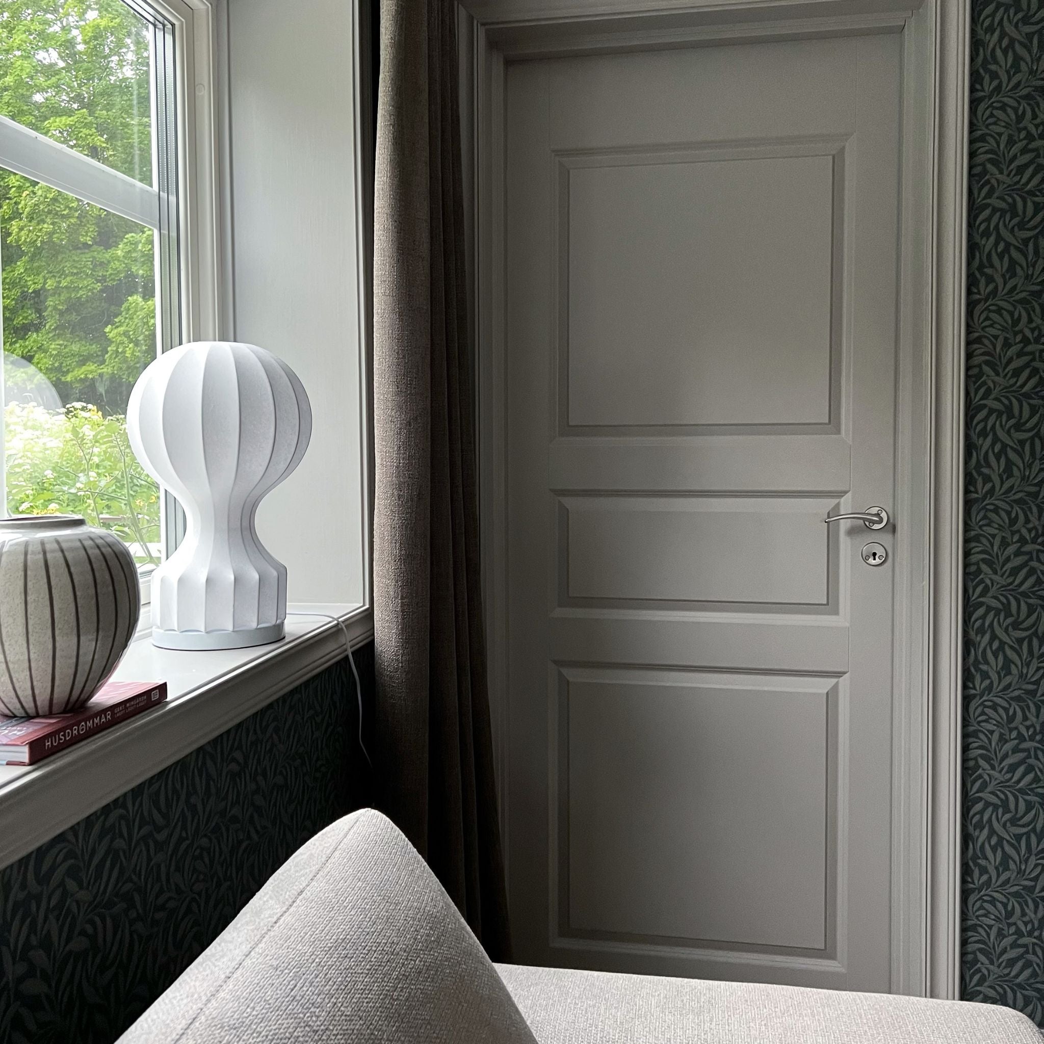Vit bordslampa i luftballongsform placerad i fönster, stilren skandinavisk inredning med naturligt ljus och mjuka textilier.