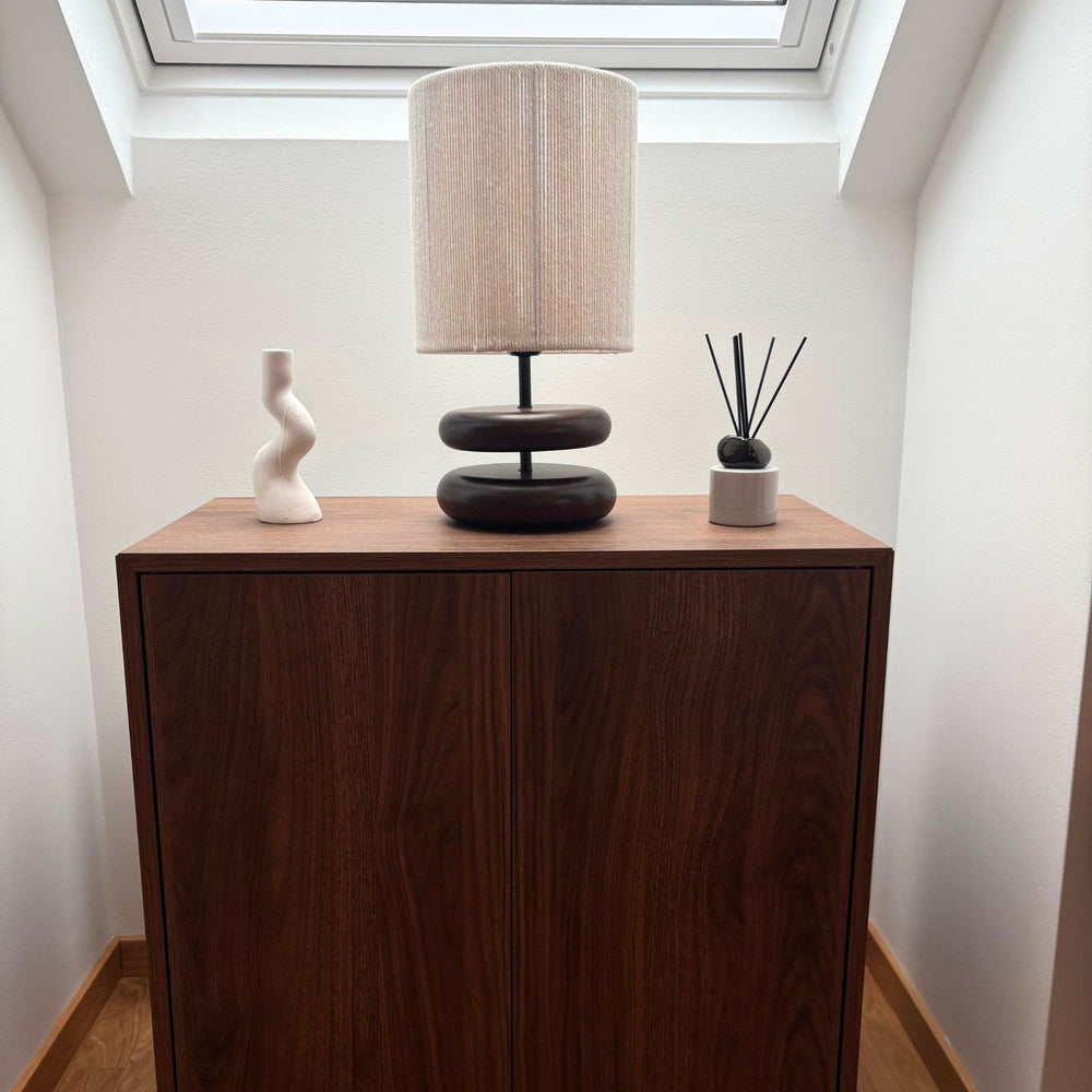 Bordslampa i mörkt trä med beige linneskärm på träskåp i ljus hall