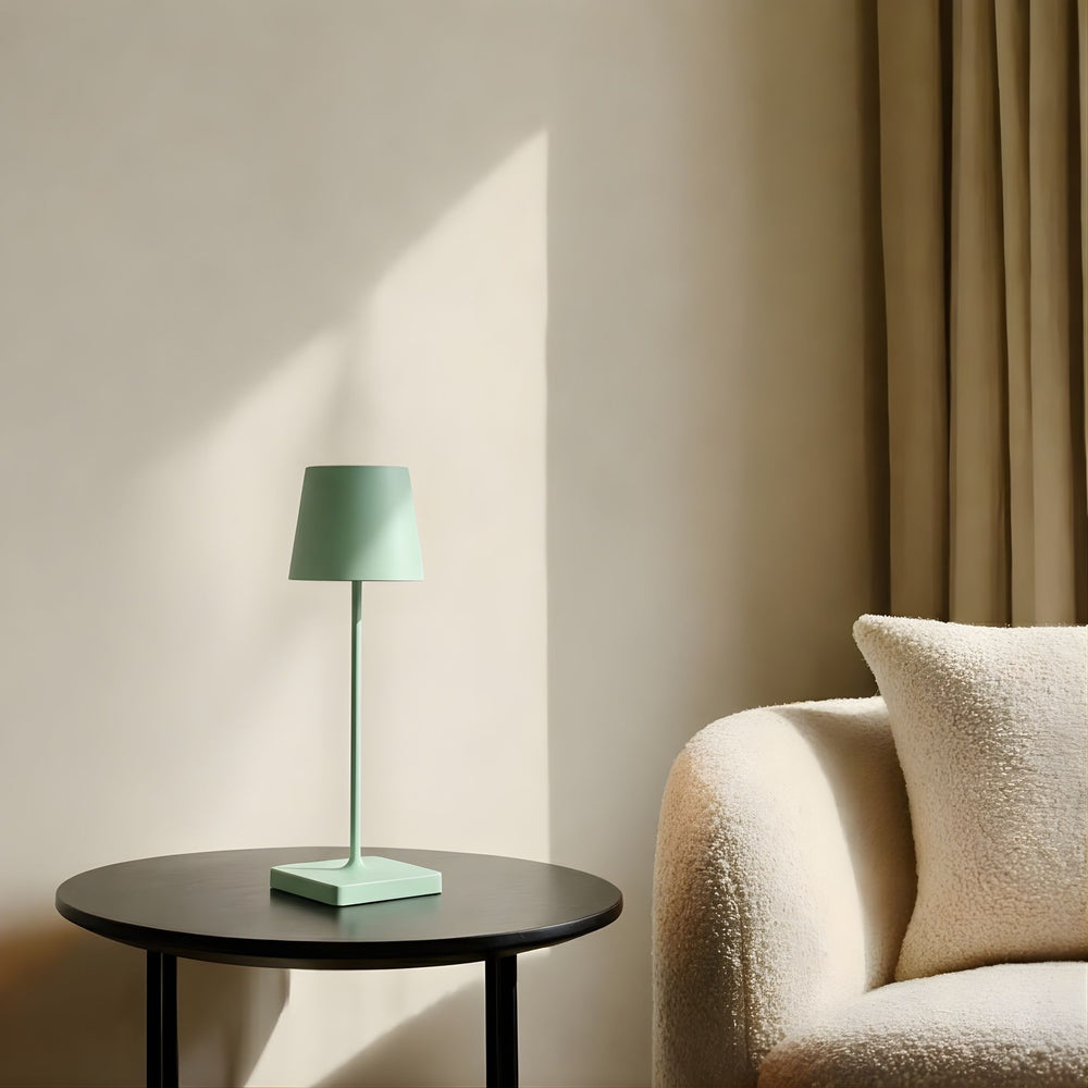 Oslo bordslampa i grön finish på runt sidobord bredvid fåtölj i ljust vardagsrum med varma skuggor och skandinavisk design.