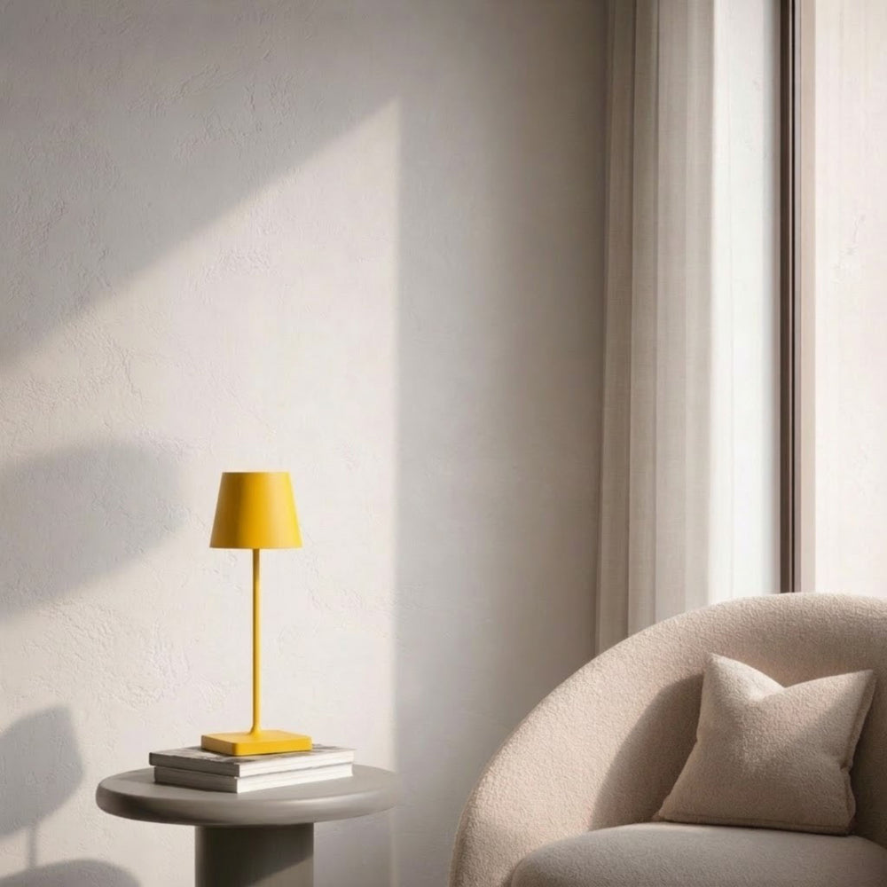 Oslo bordslampa i gul färg placerad på runt sidobord ovanpå böcker bredvid fåtölj i ljust vardagsrum med mjuka textilier och skandinavisk inredning.
