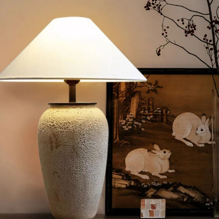 Bordslampa Terra i naturfärger - placerad i harmonisk interiör med konst och mjuk belysning.