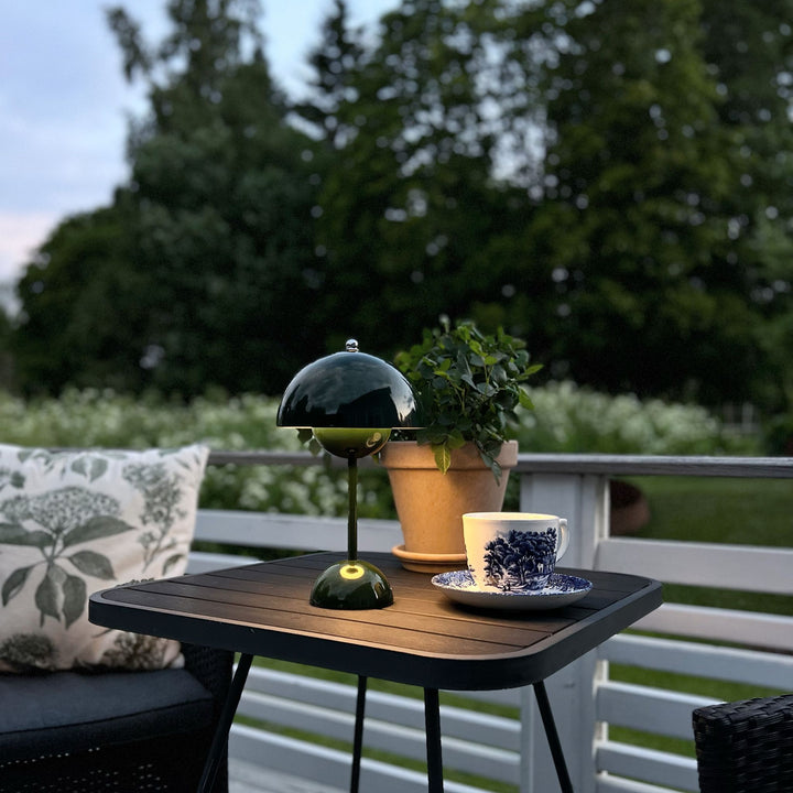 Grön Flowerbud Portabel bordslampa använd som stämningsbelysning på altanbord i utomhusmiljö under kvällstid.