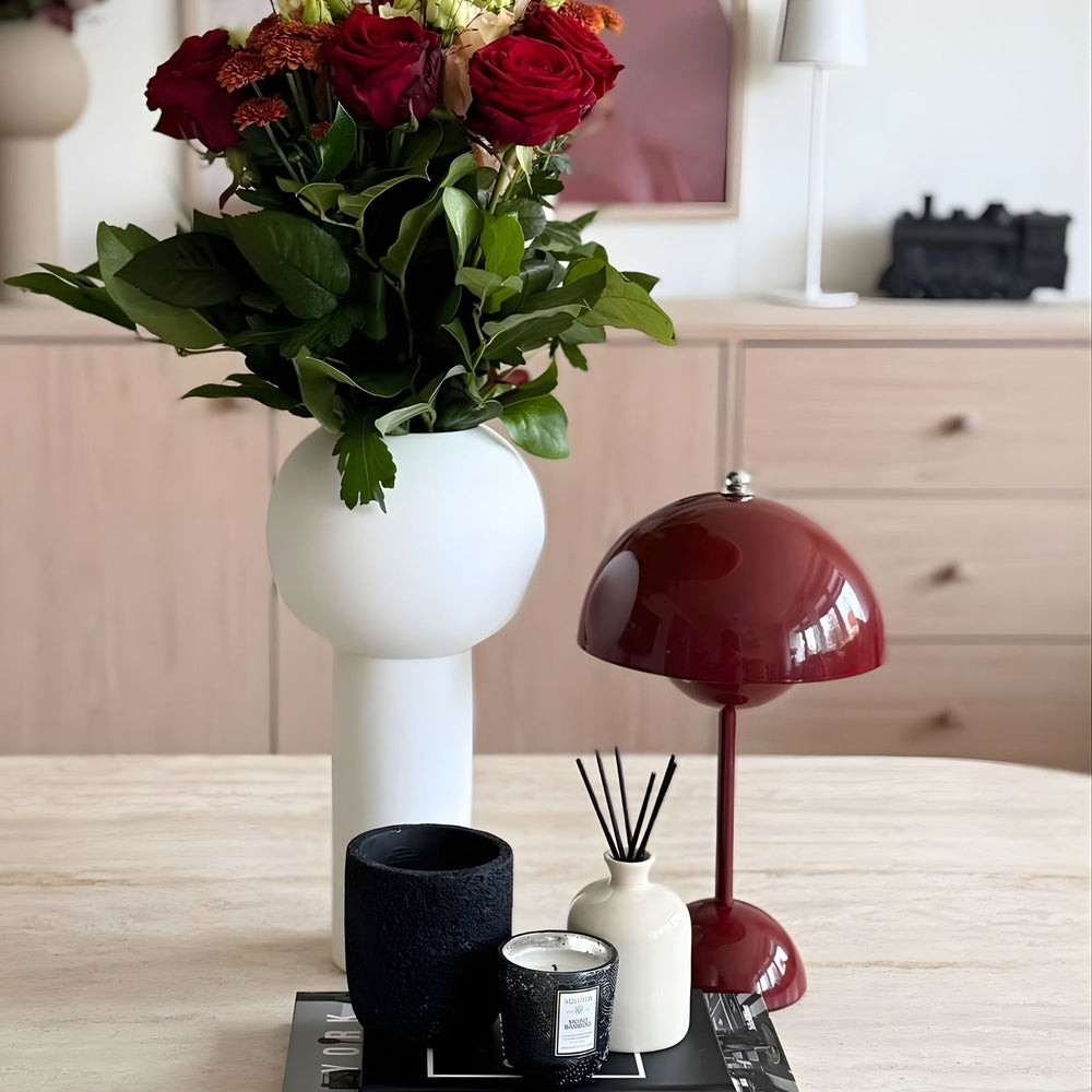 Flowerbud bordslampa i röd placerad bredvid en vad med rosor på matbord som dekorativ designbelysning i skandinavisk inredning.