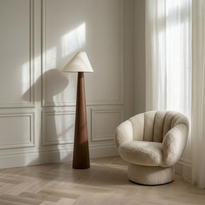 Golvlampa Timber med konformad träbas och vit lampskärm placerad bredvid fåtölj i ljust skandinaviskt vardagsrum.
