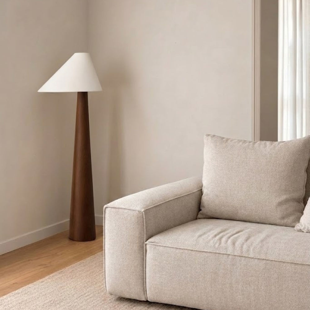 Golvlampa Timber med konformad träbas och vit lampskärm placerad bredvid soffa i ljust skandinaviskt vardagsrum