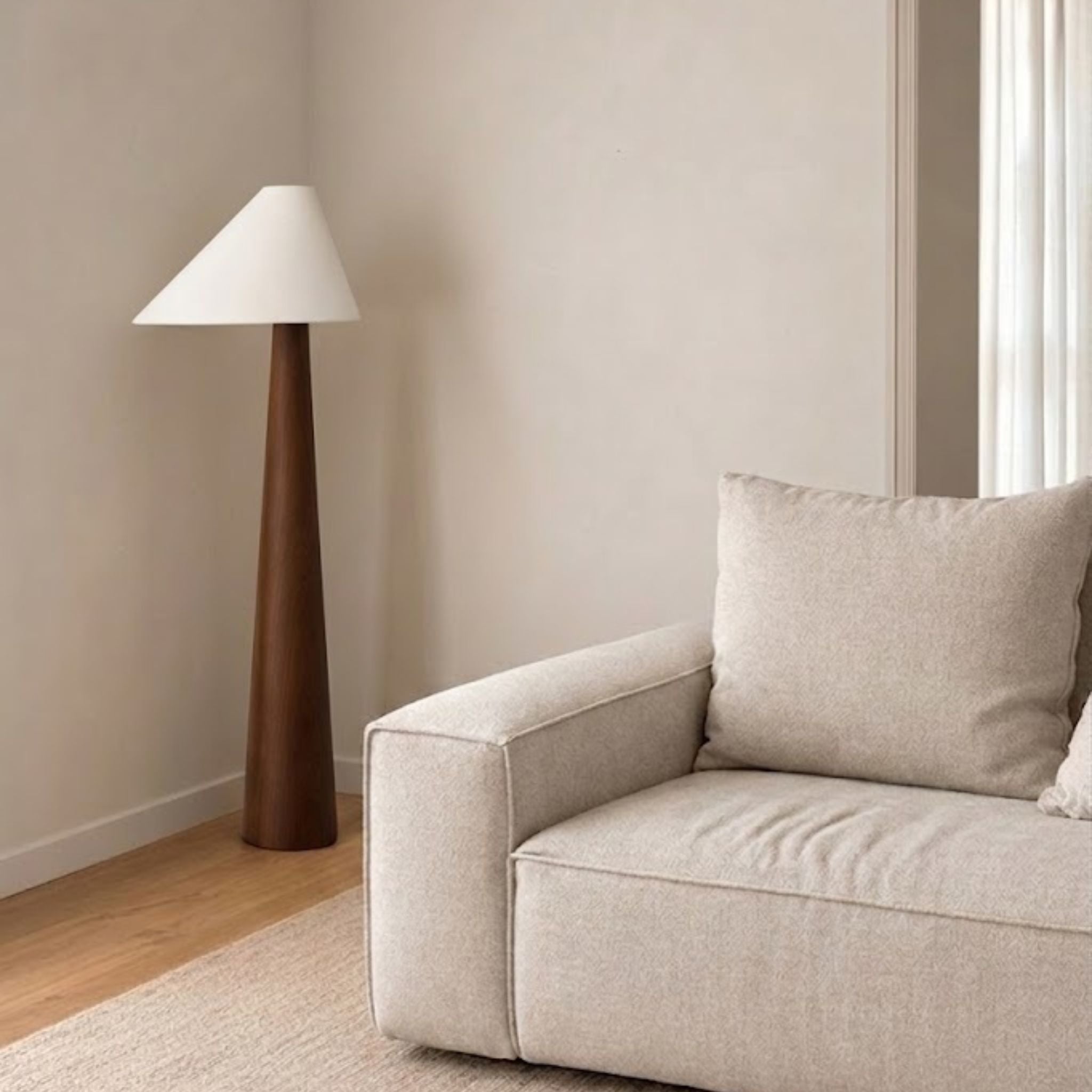 Golvlampa Timber med konformad träbas och vit lampskärm placerad bredvid soffa i ljust skandinaviskt vardagsrum