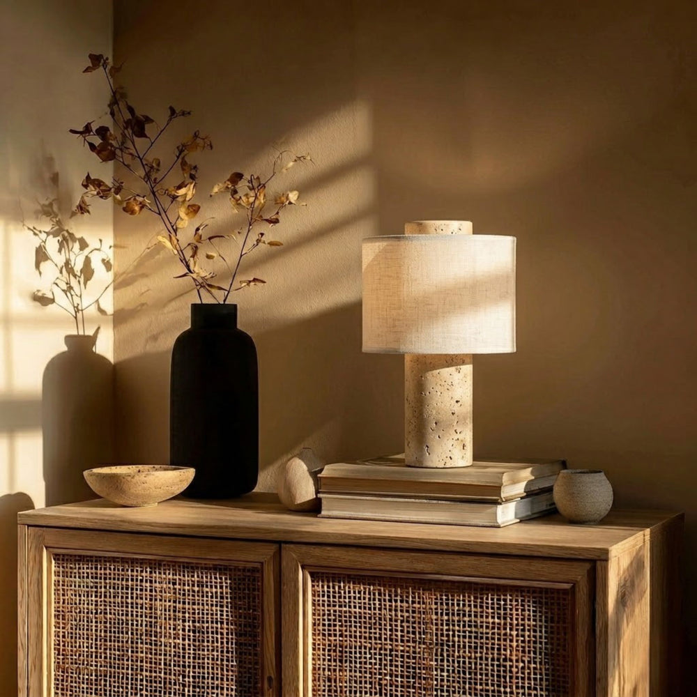 Monolit portabel bordslampa i travertin med beige linne skärm placerad på träskåp i varm skandinavisk inredning