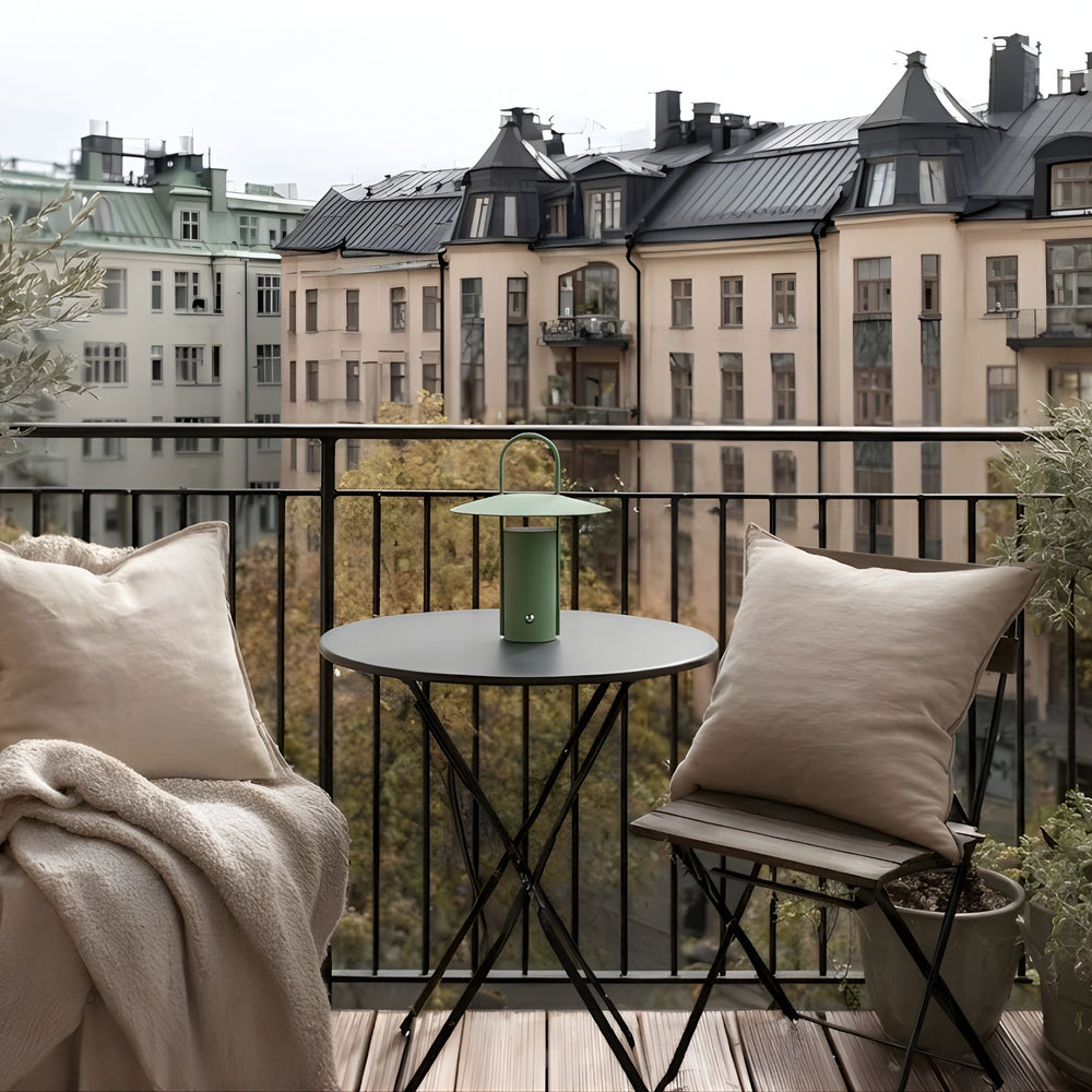 Porto portabel bordslampa i grön färg på balkongbord med utsikt över stad, omgiven av mjuka textilier och stilren skandinavisk inredning.