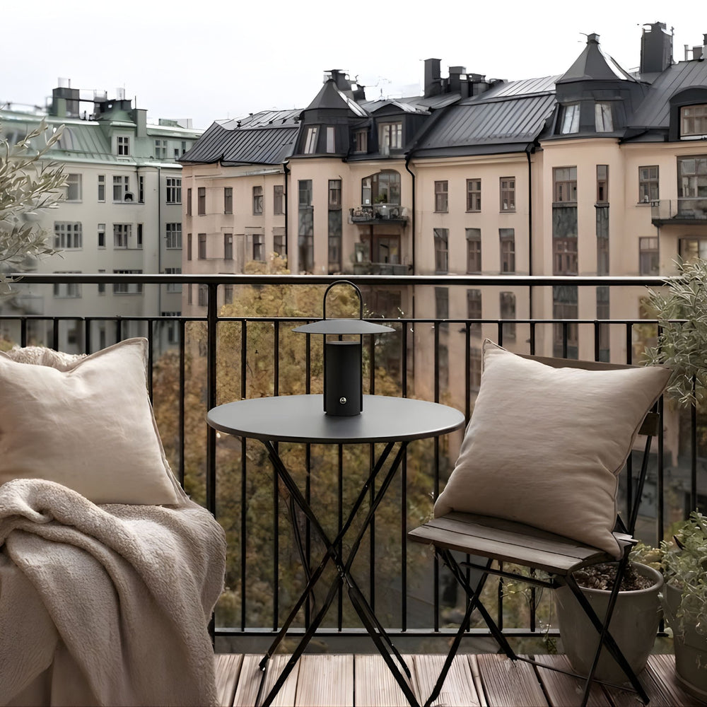 Porto portabel bordslampa i svart färg på balkongbord med utsikt över stad, omgiven av mjuka textilier och stilren skandinavisk inredning.