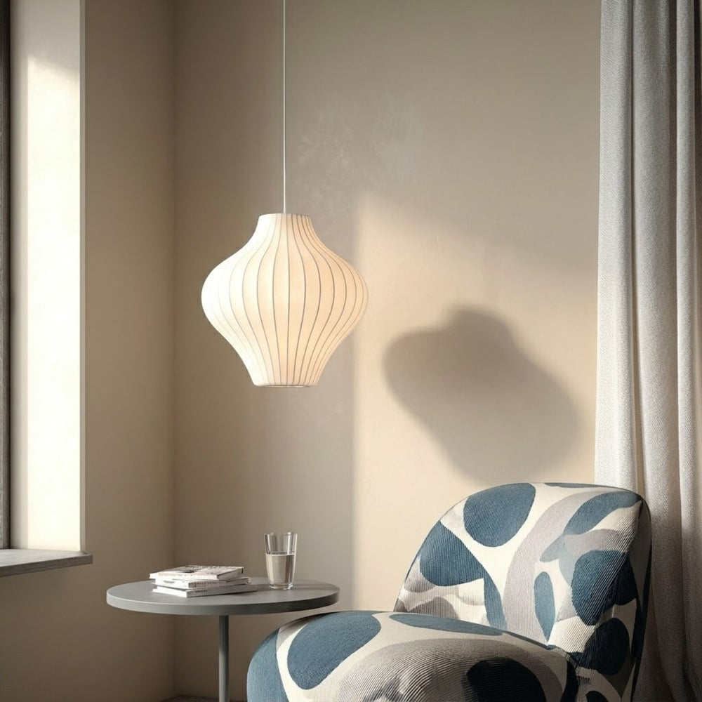 Taklampa Baluster i vit ribbad design som hänger vid fönster ovanför litet bord och fåtölj i skandinaviskt hörn – dekorativ takbelysning med mjukt varmt ljus.