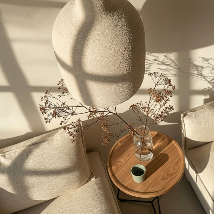 Närbild ovanifrån av Cirrus taklampa i beige textur över soffgrupp med sidobord och dekor i en varm och stilren miljö.