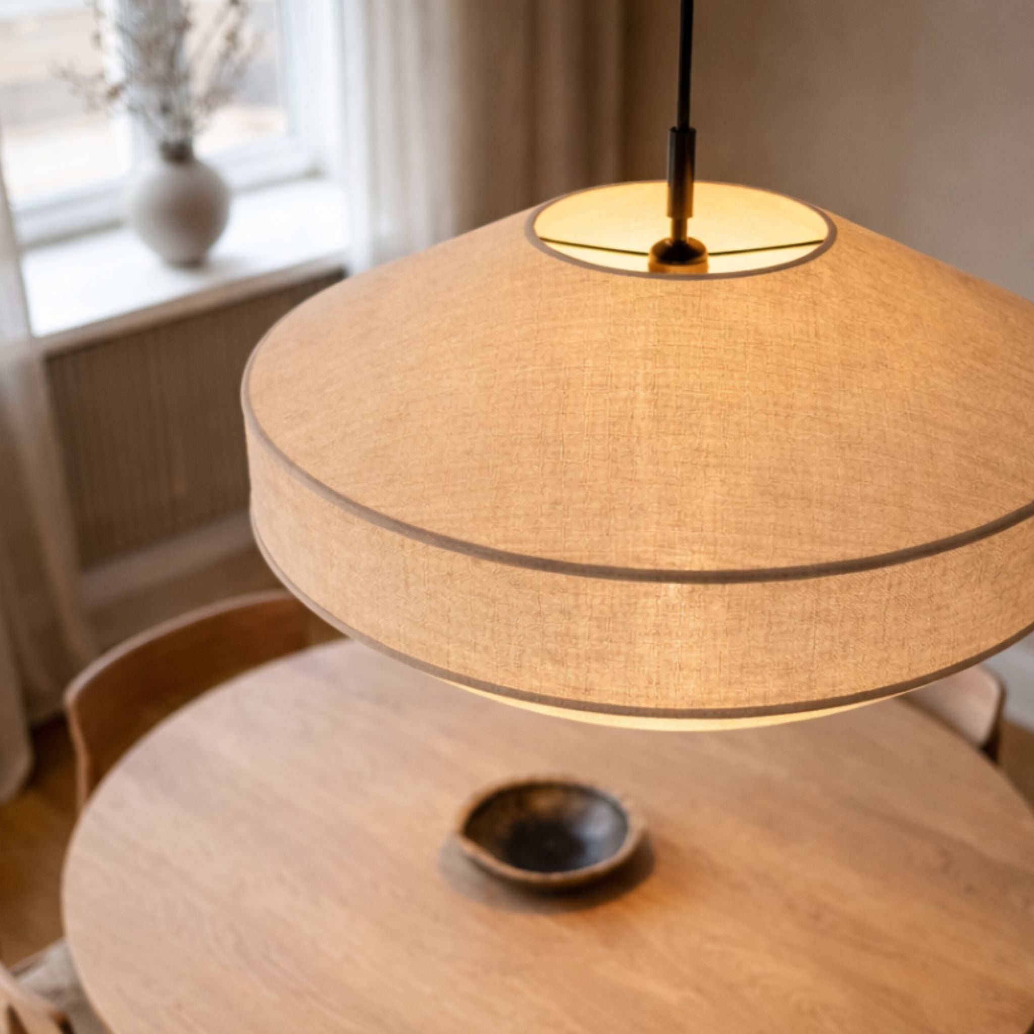 Närbild på Pagoda taklampa i beige textil med mjuk lagerdesign ovanför runt matbord i en lugn och modern miljö.
