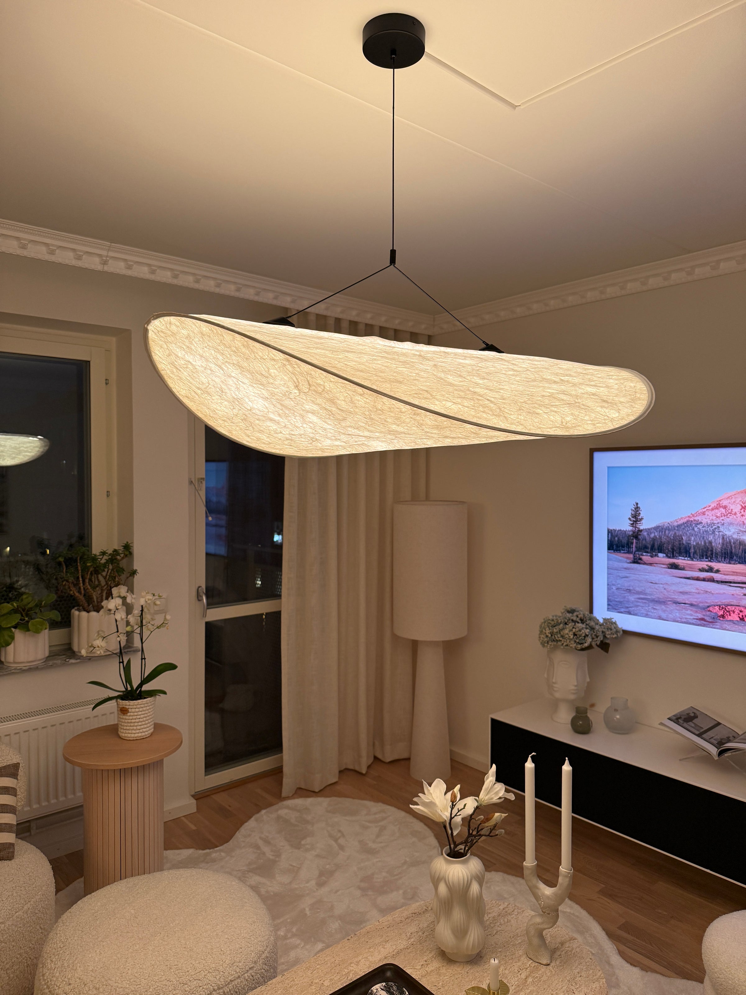 Taklampa Sailing i greige med organisk form som ger mjukt ljus över soffbord i modernt skandinaviskt vardagsrum