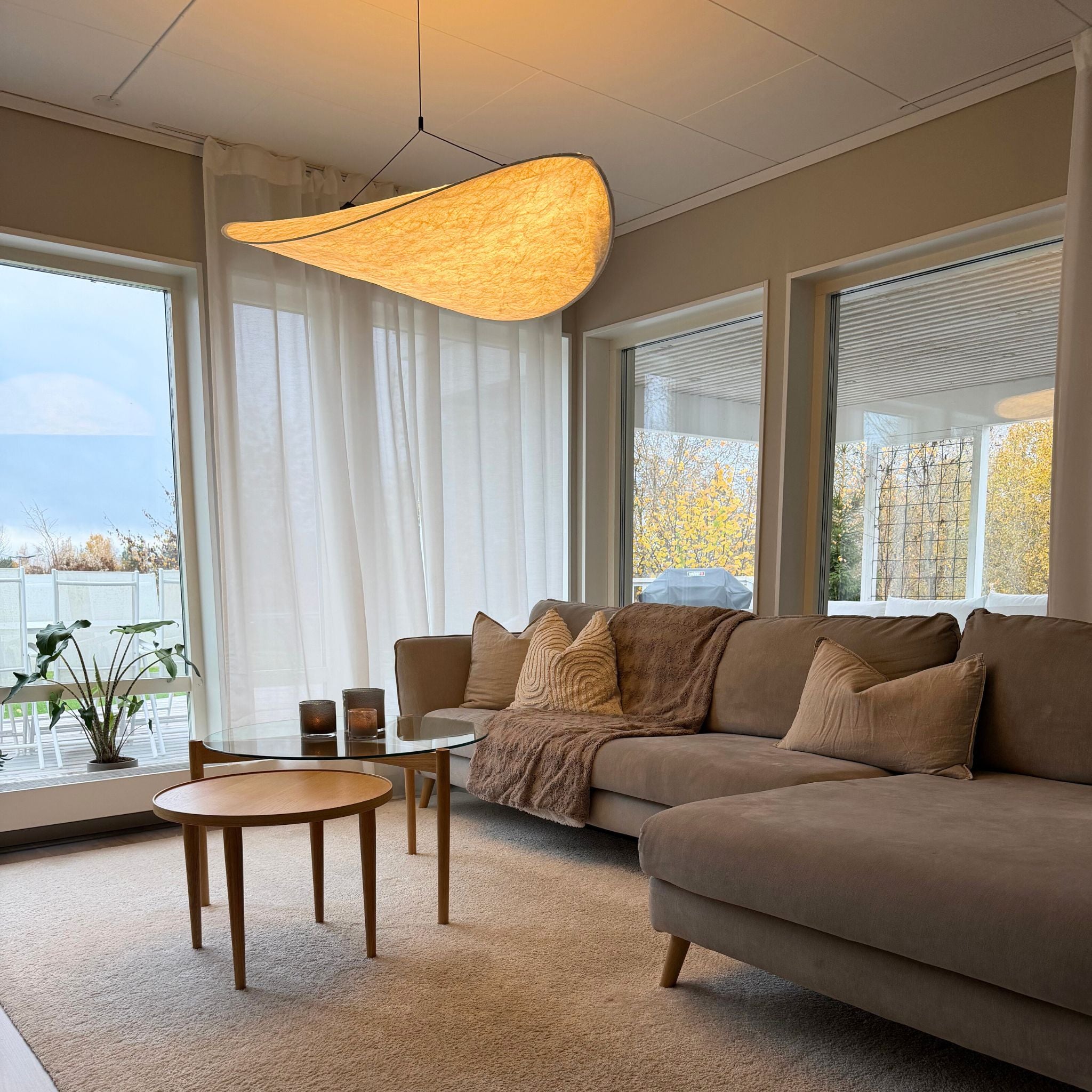 Sailing taklampa med organisk form och varm belysning, hängande i modernt vardagsrum med soffa och mjuka naturmaterial. 