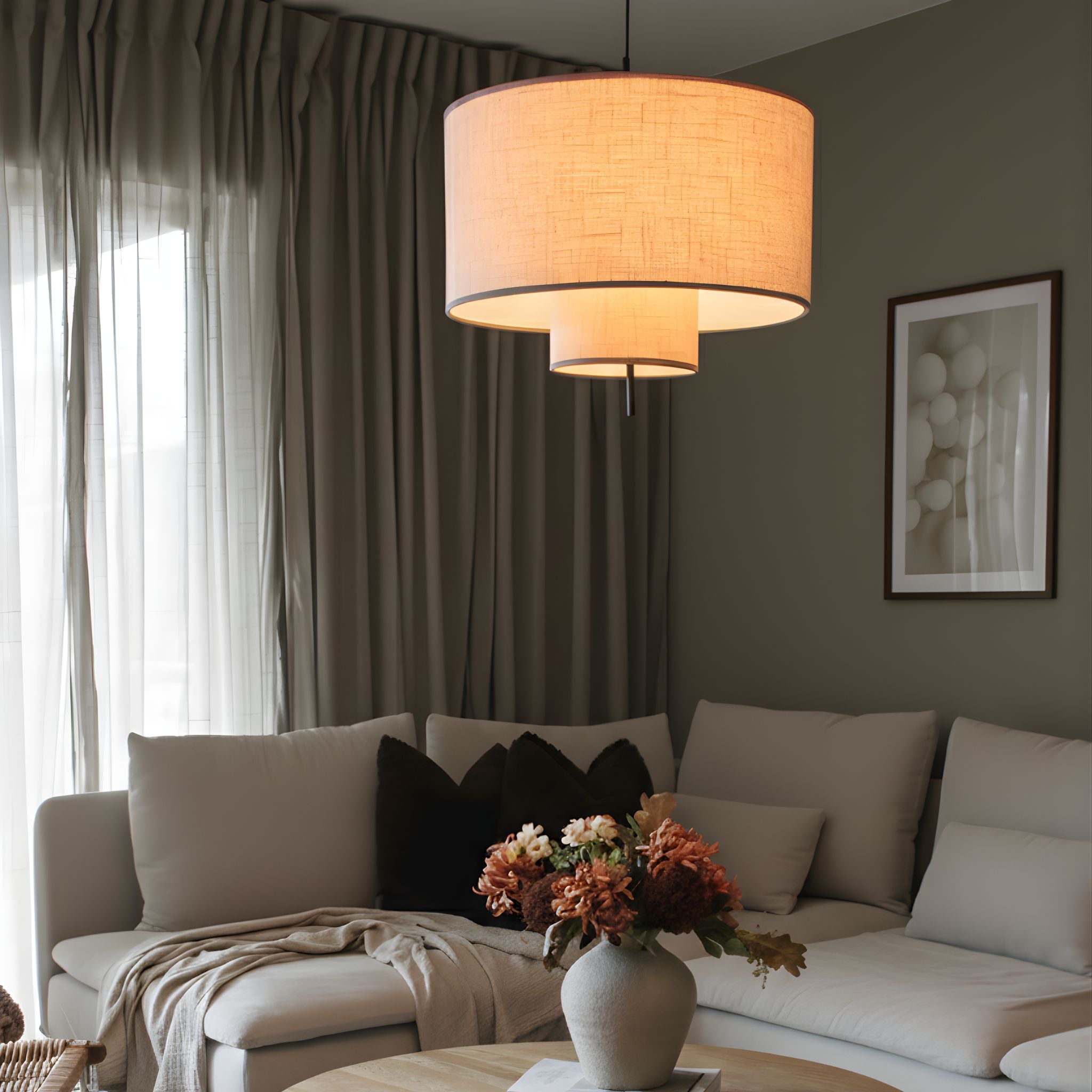 Tambour taklampa i textil med varm belysning, hängande ovanför soffbord i stilrent vardagsrum med mjuka naturtoner.